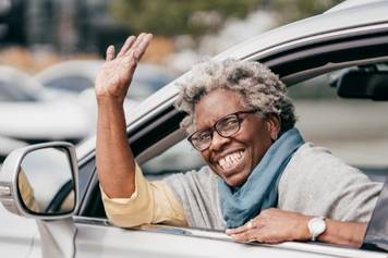 Able Hearing Beaverton - An older woman with hearing aids waving out of the window of a car.